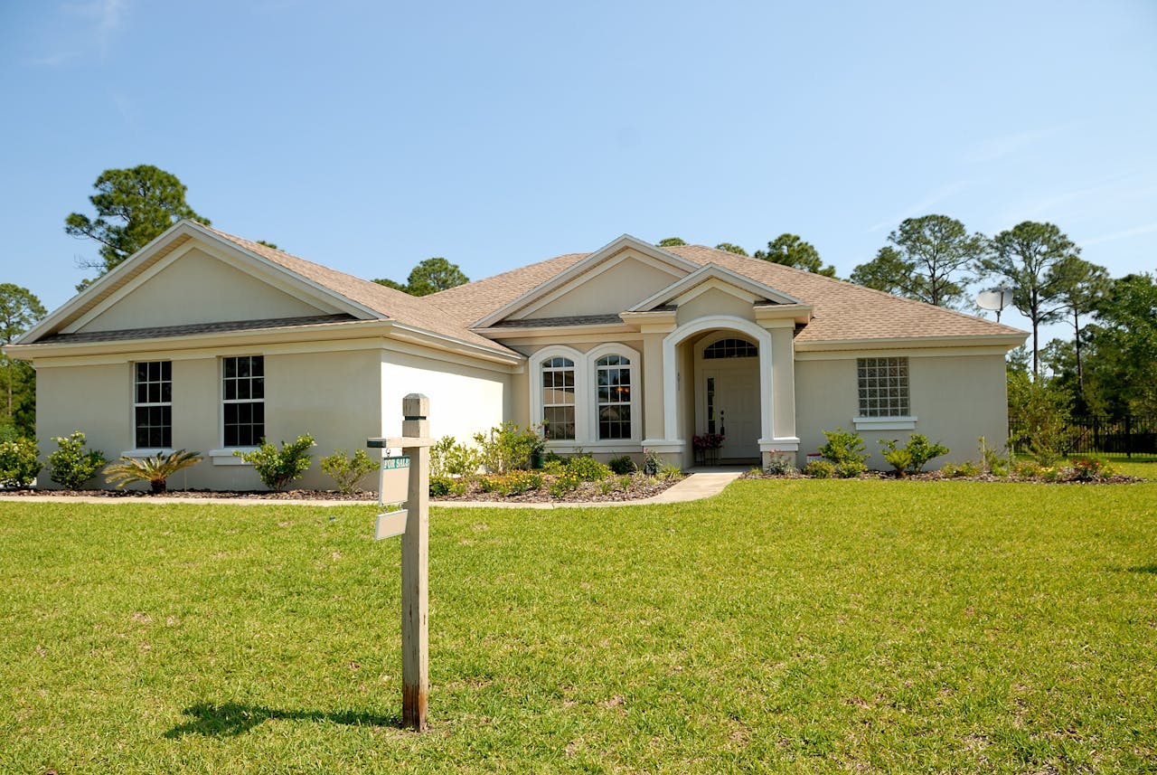 Beautiful suburban house with lush lawn, showcasing a for sale sign under a clear blue sky.